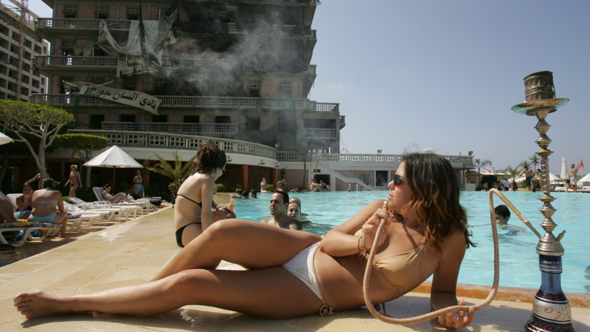 A Lebanese woman smokes a waterpipe, locally known as nargileh, next to the swimming pool of Beirut's landmark Saint-Georges hotel (background) 05 June 2005. Lebanon's former premier Rafiq Hariri was assassinated in a massive car bomb explosion outside the hotel on February 14. The owner of the hotel, Fady Khoury, was slightly wounded in the attack which he said cost him losses worth millions of dollars. The hotel, overlooking the Mediterranean, had been badly damaged during the famous 'hotels battle' in 1976 at the start of the Lebanese civil war and was still under reconstruction. Only the pool area has been refurbished and open to the public.  AFP PHOTO/PATRICK BAZ        (Photo credit should read PATRICK BAZ/AFP/Getty Images)