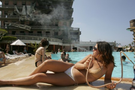 A Lebanese woman smokes a waterpipe, locally known as nargileh, next to the swimming pool of Beirut's landmark Saint-Georges hotel (background) 05 June 2005. Lebanon's former premier Rafiq Hariri was assassinated in a massive car bomb explosion outside the hotel on February 14. The owner of the hotel, Fady Khoury, was slightly wounded in the attack which he said cost him losses worth millions of dollars. The hotel, overlooking the Mediterranean, had been badly damaged during the famous 'hotels battle' in 1976 at the start of the Lebanese civil war and was still under reconstruction. Only the pool area has been refurbished and open to the public.  AFP PHOTO/PATRICK BAZ        (Photo credit should read PATRICK BAZ/AFP/Getty Images)