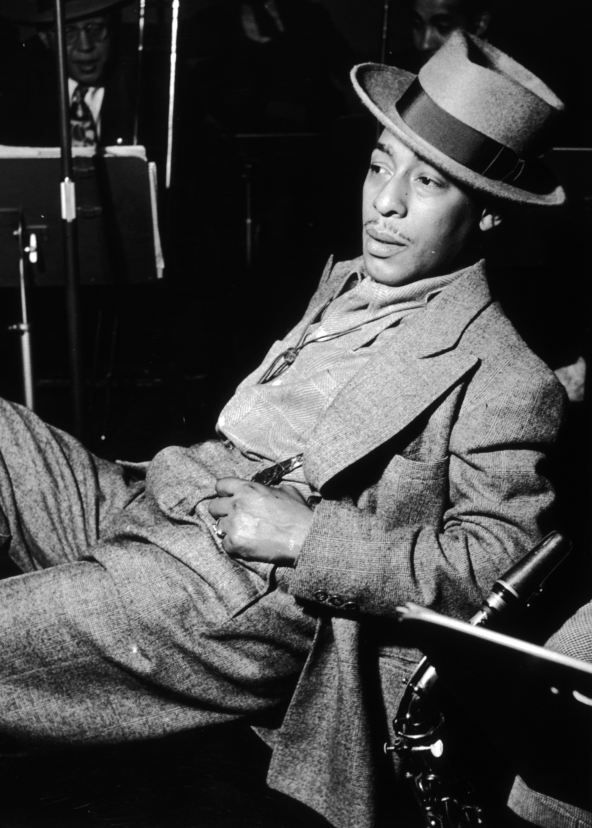 circa 1945: EXCLUSIVE American jazz saxophonist Johnny Hodges (1907-1970) leans back in a chair with a saxophone resting next to him. Hodges wears a suit and a felt hat. Other members of the band are seated in the background. (Photo by Metronome/Getty Images)