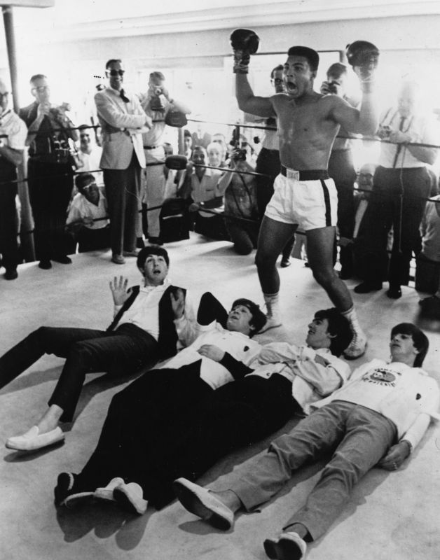February 1964: American heavyweight boxer Cassius Clay poses in the ring in mock victory over British pop group The Beatles, meeting the press in New York during an American tour. (Photo by Keystone/Getty Images)