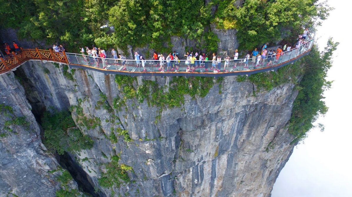 ZHANGJIAJIE, CHINA - AUGUST 01:  Aerial view of tourists walking on the 100-meter-long and 1.6-meter-wide glass skywalk clung the cliff of Tianmen Mountain (or Tianmenshan Mountain) in Zhangjiajie National Forest Park on August 1, 2016 in Zhangjiajie, Hunan Province of China. The Coiling Dragon Cliff skywalk, featuring a total of 99 road turns, layers after another, is the third glass skywalk on the Tianmen Mountain (or Tianmenshan Mountain).  (Photo by VCG/VCG via Getty Images)