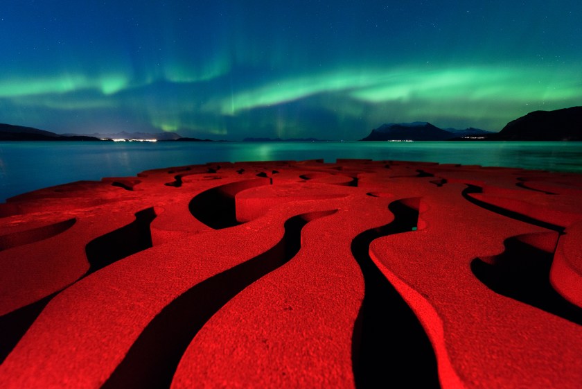 The rusty red swirls of the circular, iron sculpture Seven Magic Points in Brattebergan, Norway mirror the rippling aurora above. (Rune Engebo)