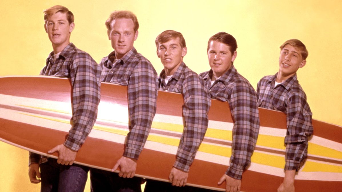 LOS ANGELES - AUGUST 1962: Rock and roll band "The Beach Boys" pose for a portrait with a surfboard in August 1962 in Los Angeles, California. (L-R) Brian Wilson, Mike Love,  Dennis Wilson, Carl Wilson, David Marks. (Photo by Michael Ochs Archives/Getty Images)
