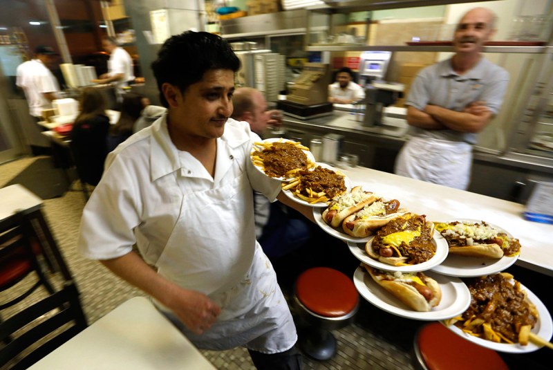 Faisal Ali delivers orders at Lafayette Coney Island in Detroit, Michigan, U.S., on Saturday, March 22, 2014. Smothered in chili sauce, mustard and onions, the Detroit-grown coney island hot dog remains a gastric constant in a city thats seen its people, businesses and, at times, its hope flee. About 140 coney islands are listed in Detroit -- many are family-style restaurants -- compared to 72 McDonalds, Burger King, Wendys and KFC franchises in the city, according to online directories and the four fast food companies. Photographer: Jeff Kowalsky/Bloomberg via Getty Images
