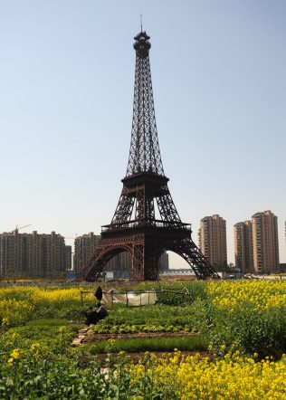 HANGZHOU, CHINA - MARCH 21: (CHINA OUT) Farmers work in front of a replica of The Eiffel Tower standing at 108 metres at Tianducheng residential community, also known as a knockoff of Paris, on March 21, 2014 in Hangzhou, China. Tianducheng is developed by Zhejiang Guangsha Co. Ltd.. The construction began in 2007 with a replica of the Eiffel Tower and Parisian houses, and it is expected to be completed by 2015. (Photo by VCG/VCG via Getty Images)