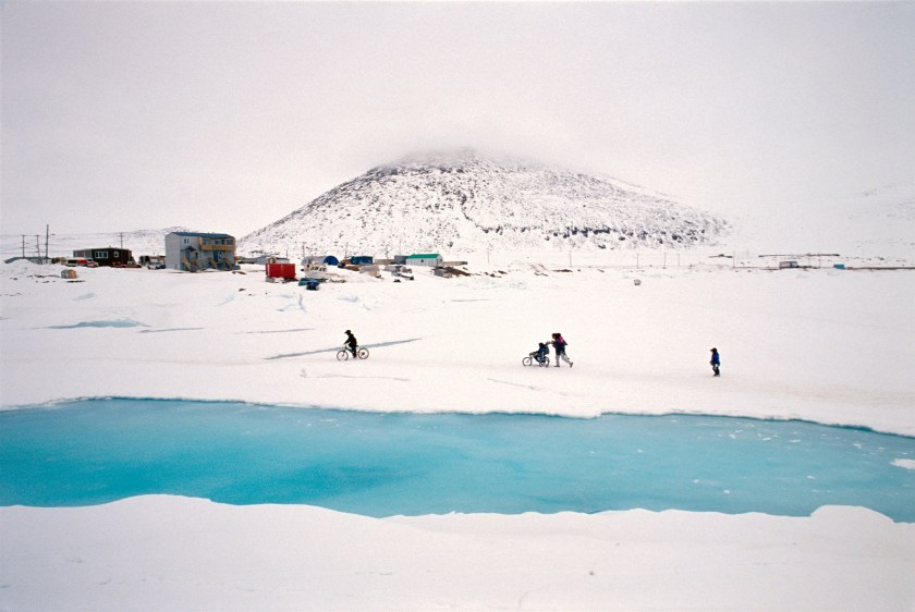 A family walking with their baby stroller on the ice of the Qikiqtarjuaq bay in Nunavut, Canada in 2004. Qikiqtarjuaq, like many Inuit villages, was a result of forced settlement of nomadic communities. Many of their problems are born from the very difficult transition from nomadism to a permanent, as found 'in the south'. (Jonas Bendiksen/Magnum Photos)