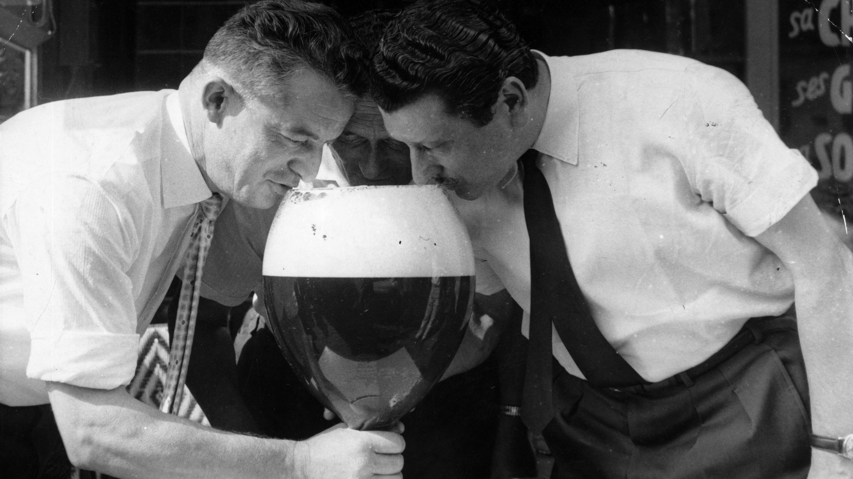 circa 1960: Three men drinking from a large glass of beer. (Photo by Keystone/Getty Images)