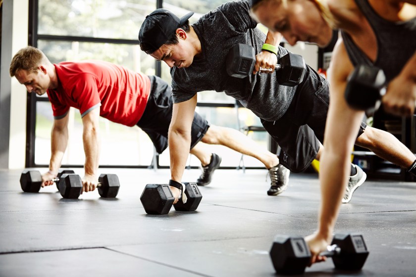 Group of friends doing pushups with dumbbells in gym (Getty Images)