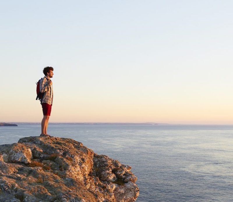 A male hiker looks towards the sunset from an Atlantic cliff.