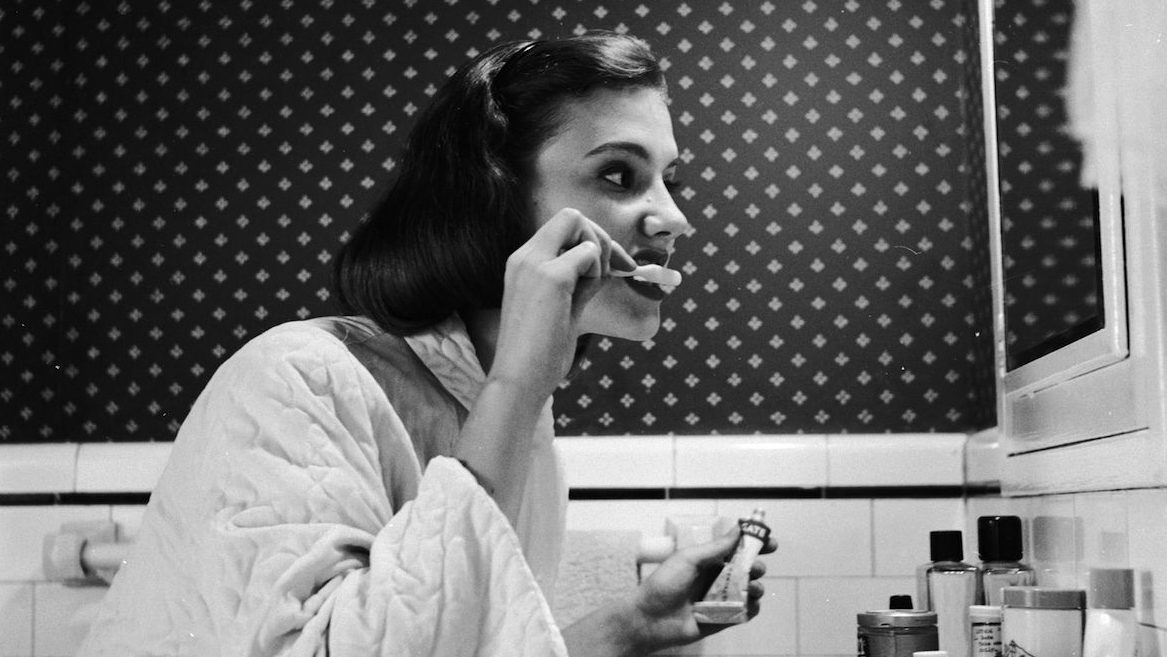 circa 1955:  A young woman brushing her teeth in her bathroom.  (Photo by Three Lions/Getty Images)