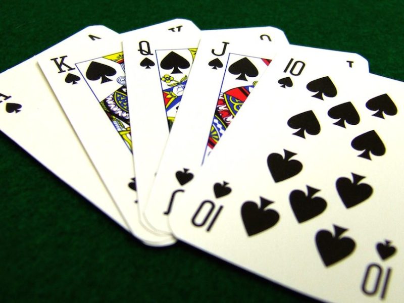Colour image of a hand of cards showing an ace high straight flush or a royal flush on a green baize background of a card table.