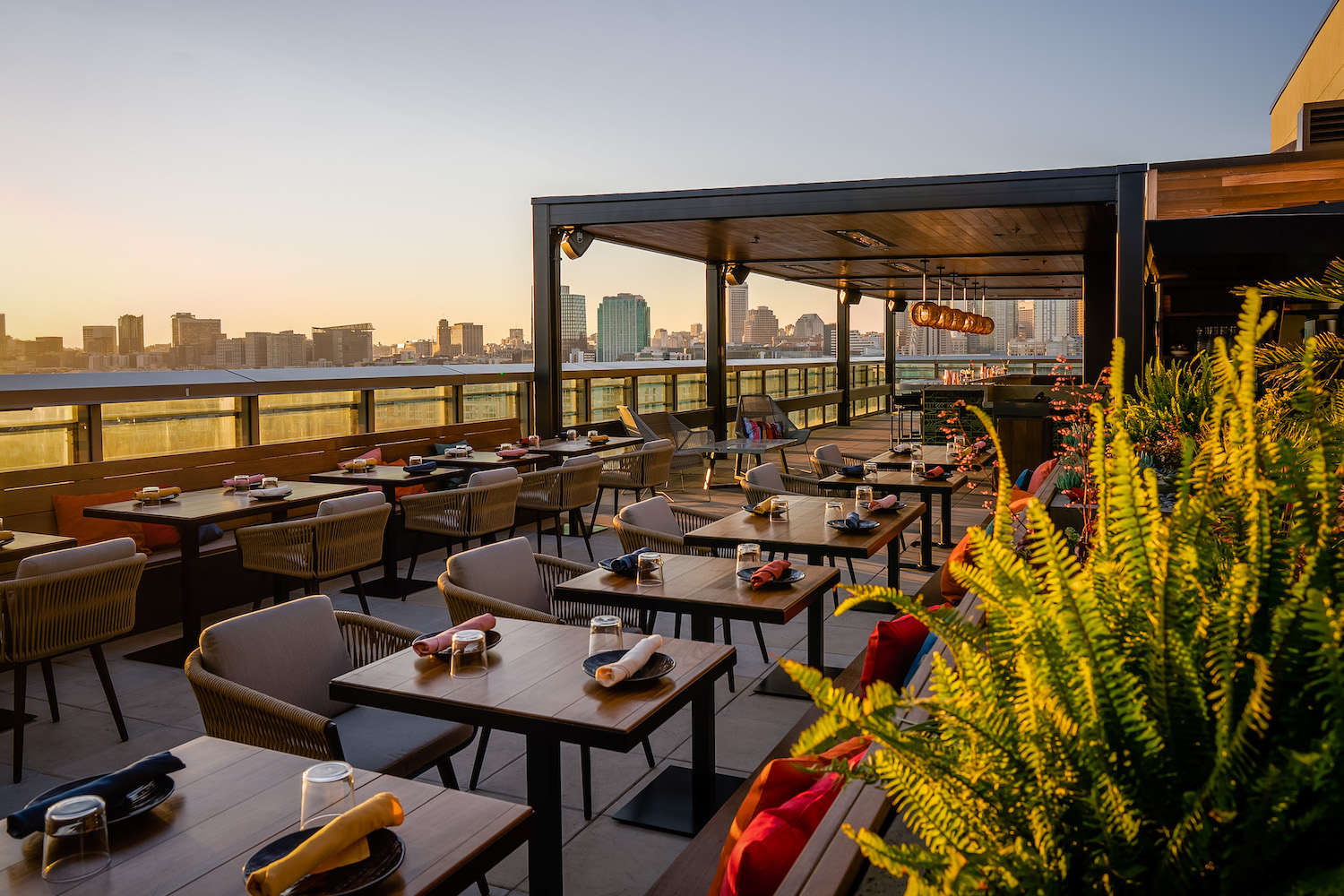 Rooftop bar area with a long row of tables, chairs and booth seats overlooking the city