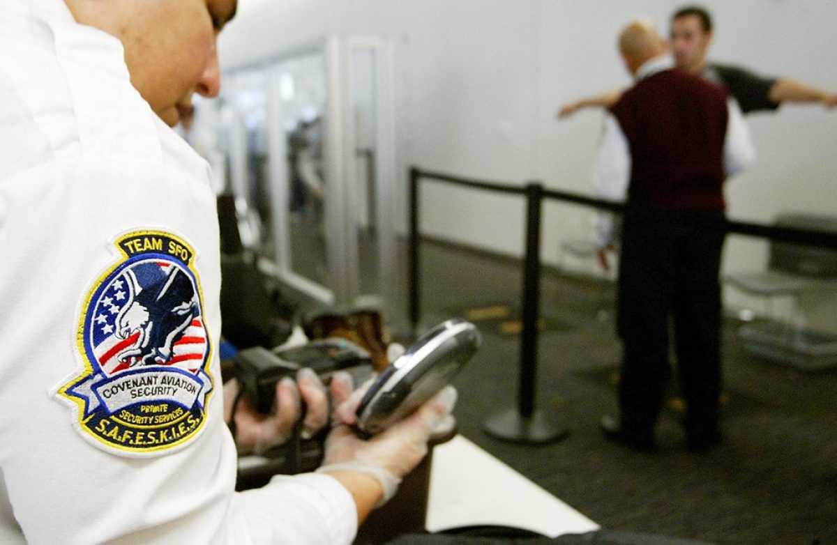 A Transportation Security Administration baggage screener inspects an electronics device as a man is screened in the background at the international terminal of San Francisco International Airport August 5, 2003 in San Francisco, California. The TSA told screeners today to pay close attention to cameras, laptop computers and cell phones, addressing a concern that terrorists could attempt to hide explosives in electronic devices. (Justin Sullivan/Getty Images)