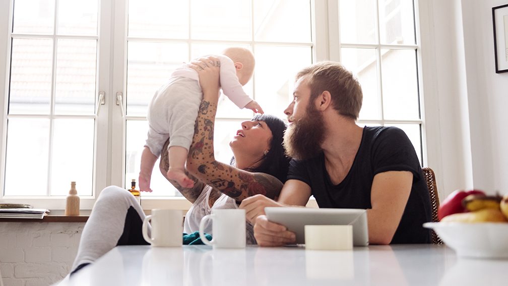 Mother and father with newborn baby sitting in their kitchen and having fun together (Getty Images)