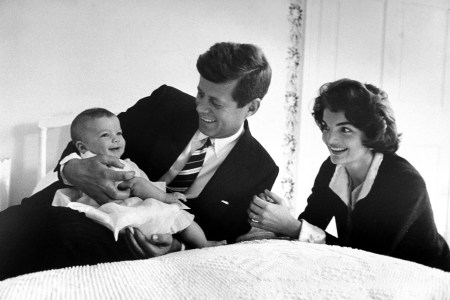 John F. Kennedy cuddling his darling baby daughter Caroline who is smiling as her mom Jackie looks on in delight while relaxing on bed at home.