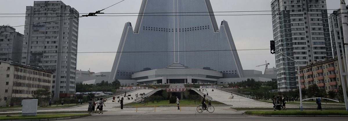 In this Friday, July 28, 2017, photo, people walk past the 105-story pyramid shaped Ryugyong Hotel in Pyongyang, North Korea. Walls set up to keep people out of a construction area around the gargantuan Ryugyong Hotel were pulled down as the North marked the anniversary of the Korean War armistice to reveal two broad new walkways leading to the building and the big red propaganda sign declaring that North Korea is a leading rocket power. (AP Photo/Wong Maye-E)