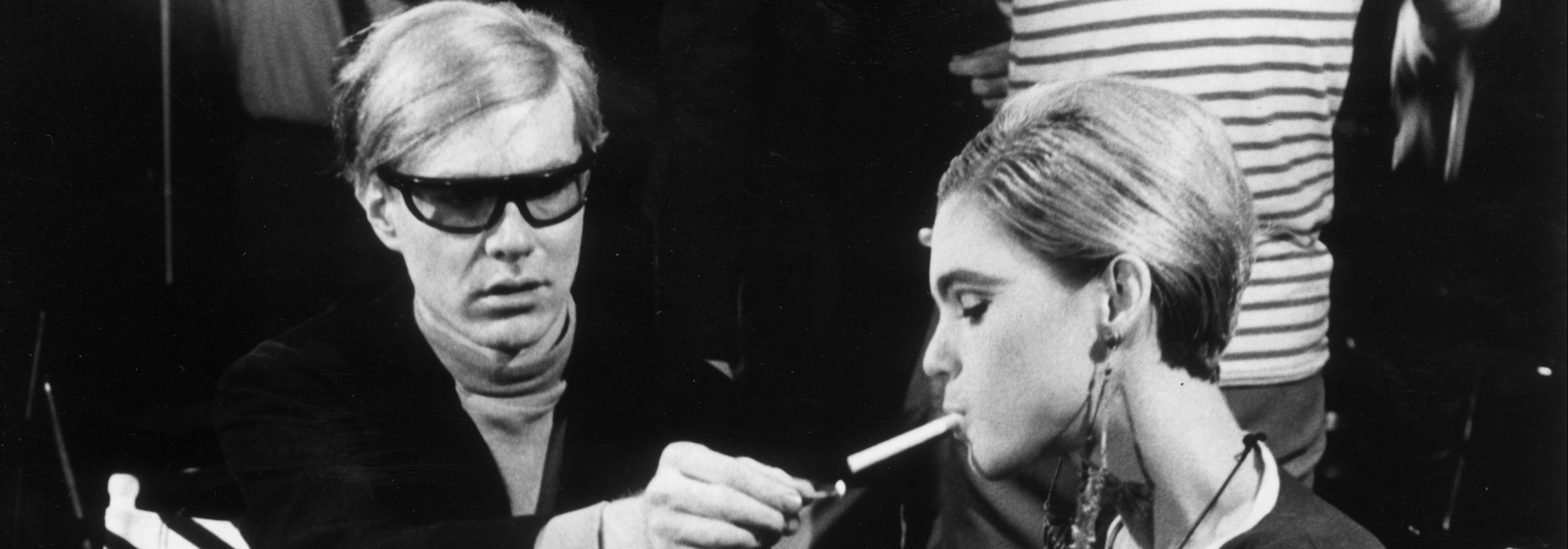 American Pop artist Andy Warhol (1928 - 1987) sits next to actor Edie Sedgwick (1943 - 1971) and lights her cigarette, on the set of one of his films.  (Walter Daran/Hulton Archive/Getty Images)