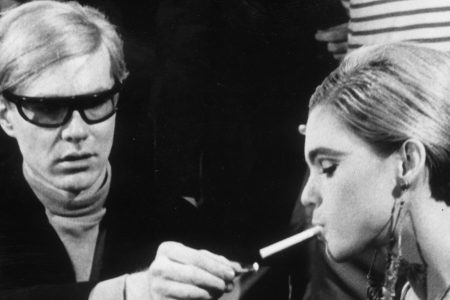 American Pop artist Andy Warhol (1928 - 1987) sits next to actor Edie Sedgwick (1943 - 1971) and lights her cigarette, on the set of one of his films.  (Walter Daran/Hulton Archive/Getty Images)