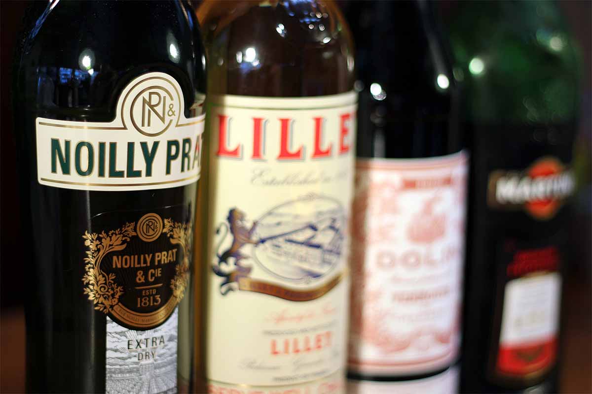A collection of vermouth and quinquina bottles, including Noilly Prat Extra Dry, Lillet Blanc, Dolin Rouge, Martini & Rossi Rosso