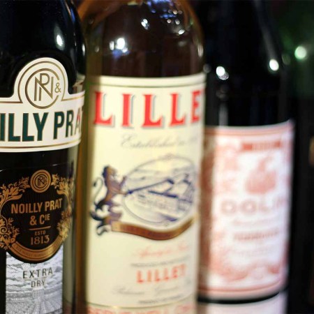 A collection of vermouth and quinquina bottles, including Noilly Prat Extra Dry, Lillet Blanc, Dolin Rouge, Martini & Rossi Rosso