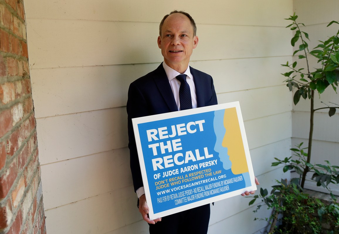 In this May 15, 2018 file photo, Judge Aaron Persky poses for a photo with a sign opposing his recall in Los Altos Hills, Calif. (AP Photo/Jeff Chiu, File)