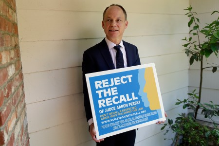 In this May 15, 2018 file photo, Judge Aaron Persky poses for a photo with a sign opposing his recall in Los Altos Hills, Calif. (AP Photo/Jeff Chiu, File)