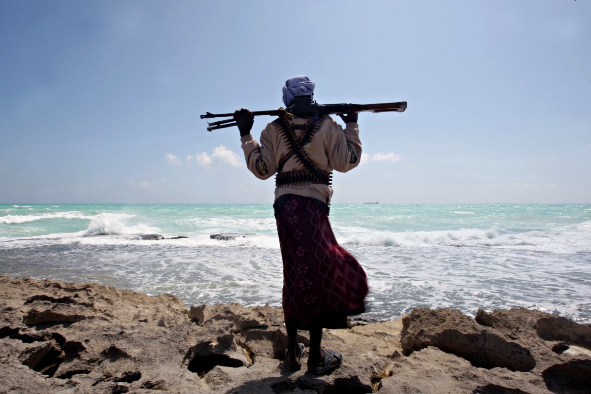 An armed Somali pirate along the coastline while the Greek cargo ship, MV Filitsa, is seen anchored just off the shores of Hobyo town in northeastern Somalia where its being held by pirates on January 7, 2010.  (AFP PHOTO/ MOHAMED DAHIR)
