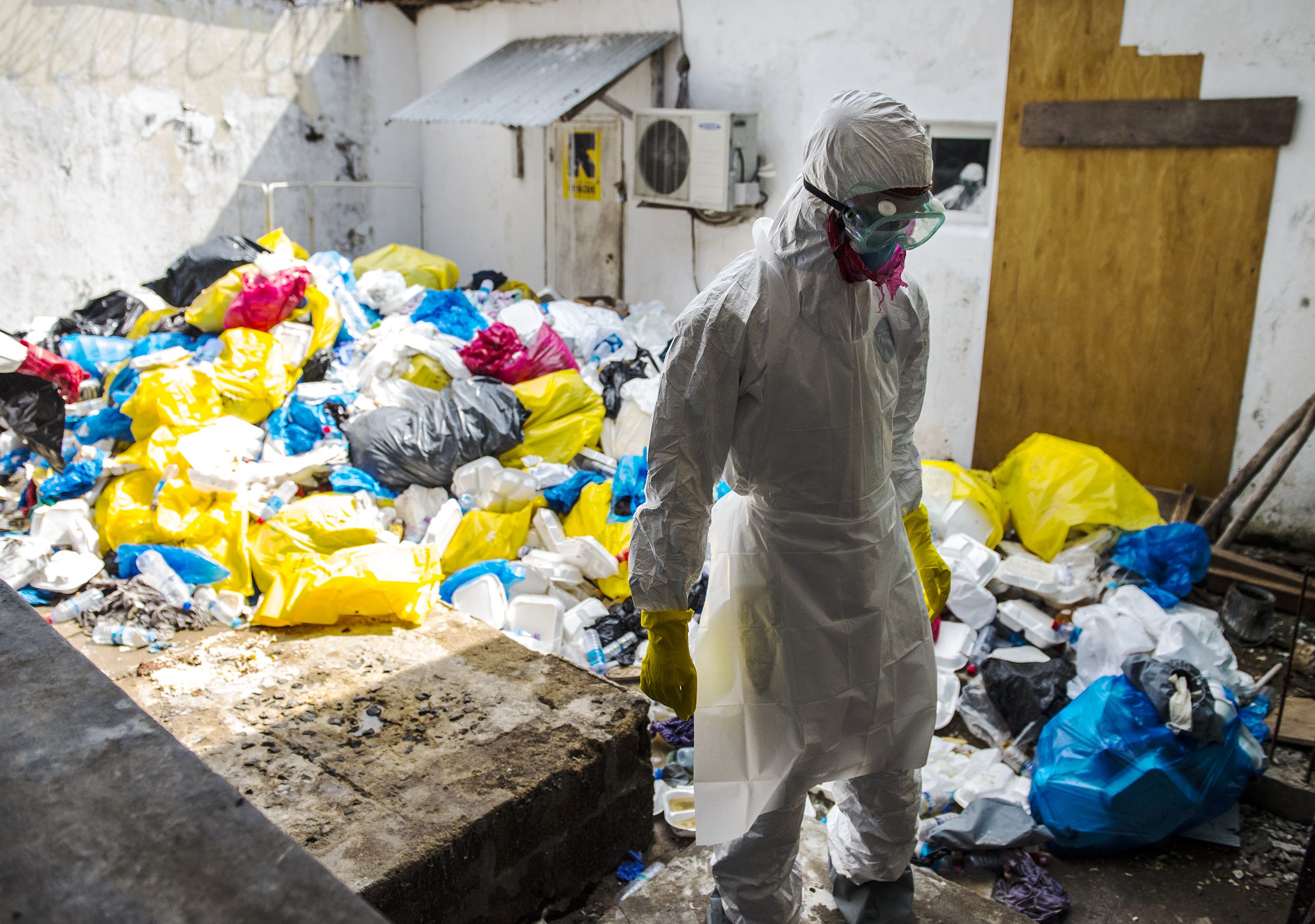 A hospital health worker stand prepares to remove garbage from Ebola patients  between wings/buildings of the Redemption  Hospital which has become a transfer and holding center to intake Ebola patients located in one of the poorest neighborhoods of Monrovia that locals call "New Kru Town on Saturday September 20, 2014 in Monrovia, Liberia. (Photo by Michel du Cille/The Washington Post via Getty Images)