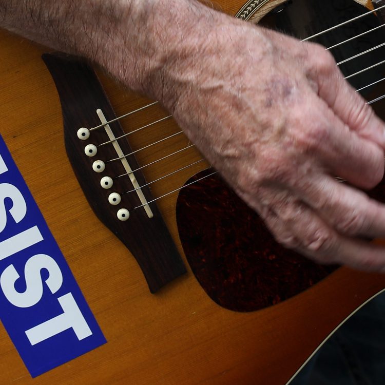 With his guitar adorned with a 'RESIST' sticker, a demonstrator plays music during a gathering to mark the 73rd anniversary of the Hiroshima and Nagasaki nuclear bombings, outside the Japanese Consulate in Midtown Manhattan, August 3, 2018 in New York City. (Photo by Drew Angerer/Getty Images)