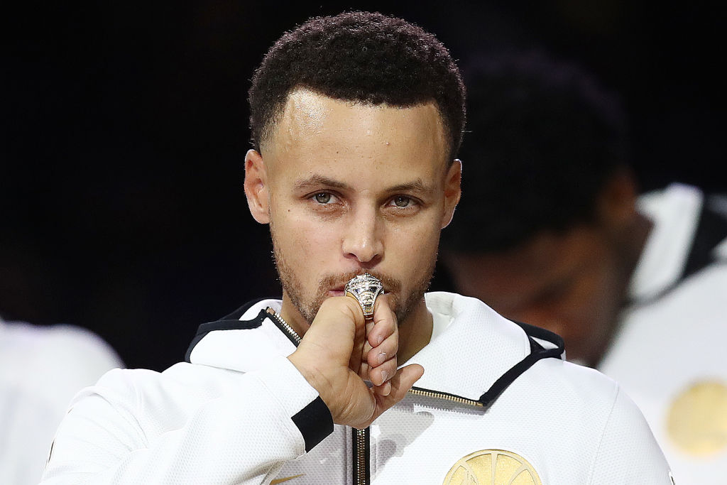 OAKLAND, CA - OCTOBER 16: Stephen Curry #30 of the Golden State Warriors kisses at his 2017-2018 Championship ring prior to their game against the Oklahoma City Thunder at ORACLE Arena on October 16, 2018 in Oakland, California.  (Photo by Ezra Shaw/Getty Images)