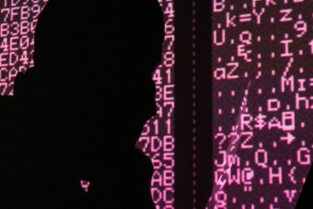 A silhouette of a man in a balaclava mask sitting at a laptop computer, with computer code in the background. Sergei Konkov/TASS (Photo by Sergei KonkovTASS via Getty Images)