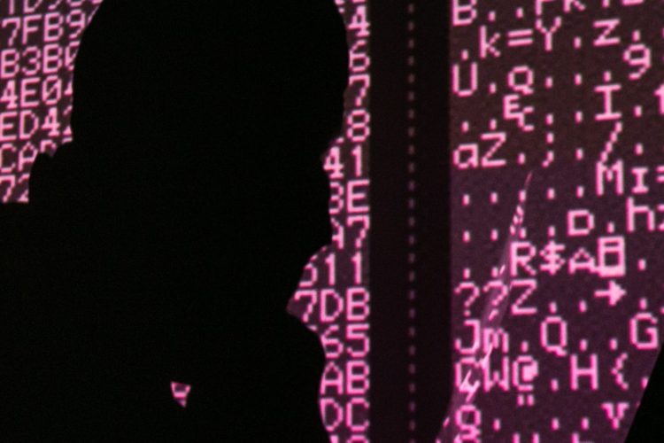 A silhouette of a man in a balaclava mask sitting at a laptop computer, with computer code in the background. Sergei Konkov/TASS (Photo by Sergei KonkovTASS via Getty Images)