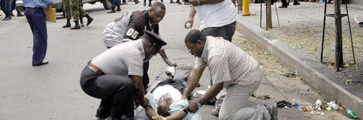 Police and pedestrians help a man wounded 11 July, 2005 after an explosive artifact exploded in a busy shopping district in downtown Port-of-Spain, Trinidad and Tobago, wounding 13 people. Police have yet to confirm if the blast was caused by a bomb or a hand grenade thrown into the bin, as some eyewitness reported.  AFP PHOTO STR   MAXIMUM QUALITY AVAILABLE  TRINIDAD AND TOBAGO OUT  (Photo credit should read STR/AFP/Getty Images)