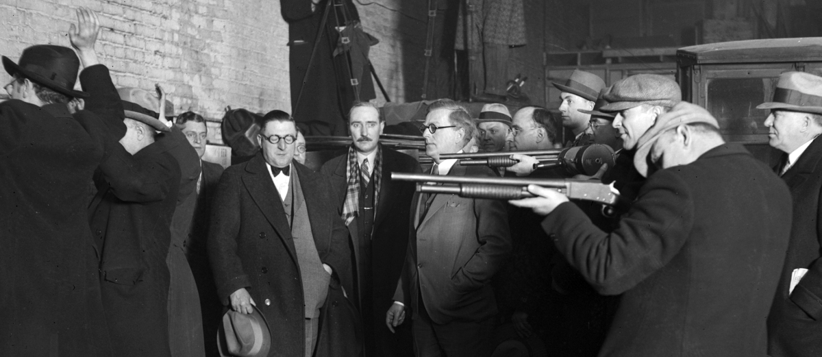 UNITED STATES - FEBRUARY 01: Police reenactment of the St. Valentine's Day Massacre, also known as the Moran Gang Massacre, when reputed members of the Al Capone gang disguised themselves as policemen and murdered members of the George 'Bugs' Moran gang in a garage at 2122 North Clark Street in the Lake View community area of Chicago, Illinois. Dr. Herman N. Bundesen, Cook County Coroner, is standing next to the men holding the rifles. (Photo by Chicago Sun-Times/Chicago Daily News collection/Chicago History Museum/Getty Images)