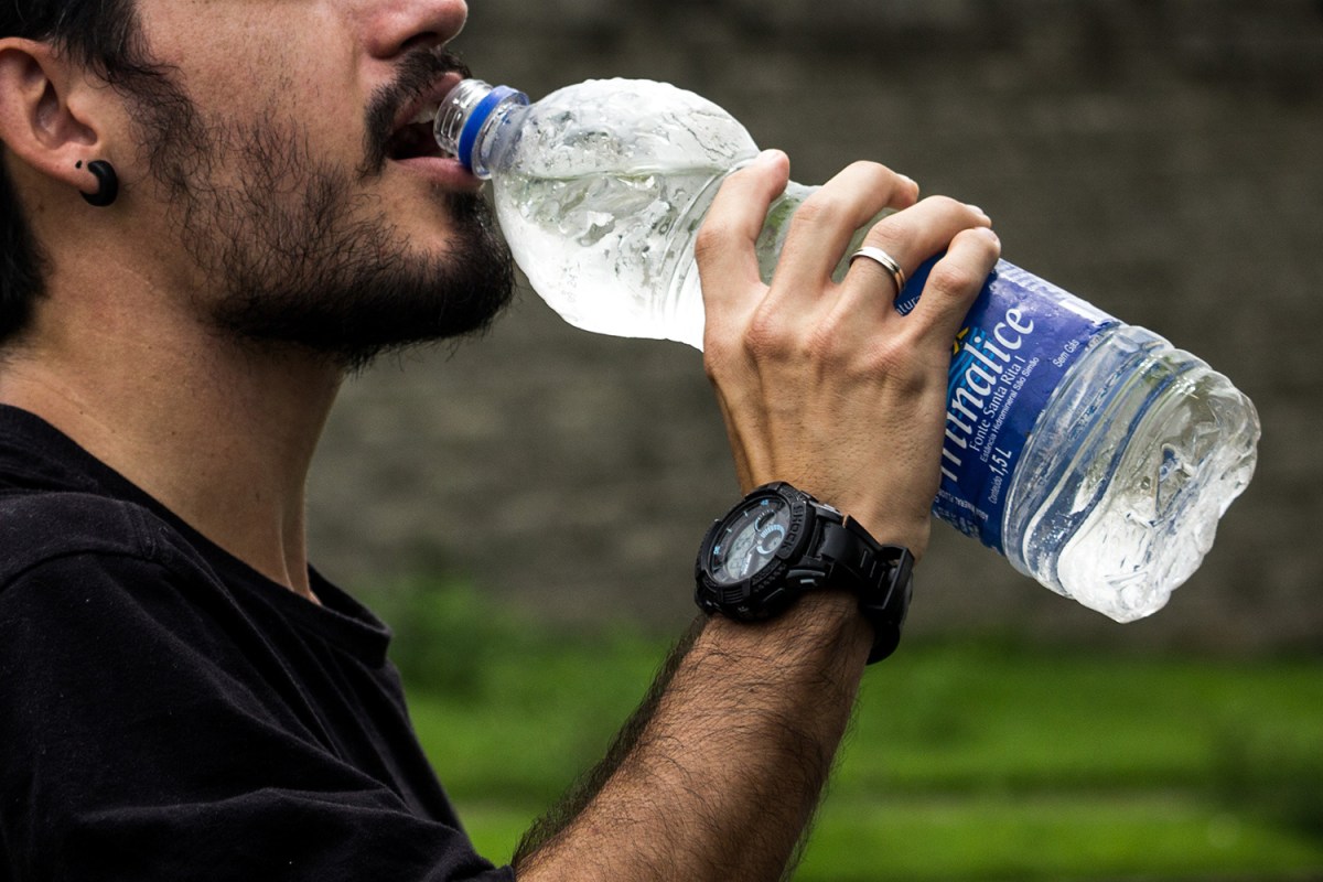 A man drinking from a plastic bottle of water. We need to stop drinking bottled water to save the planet and ourselves.