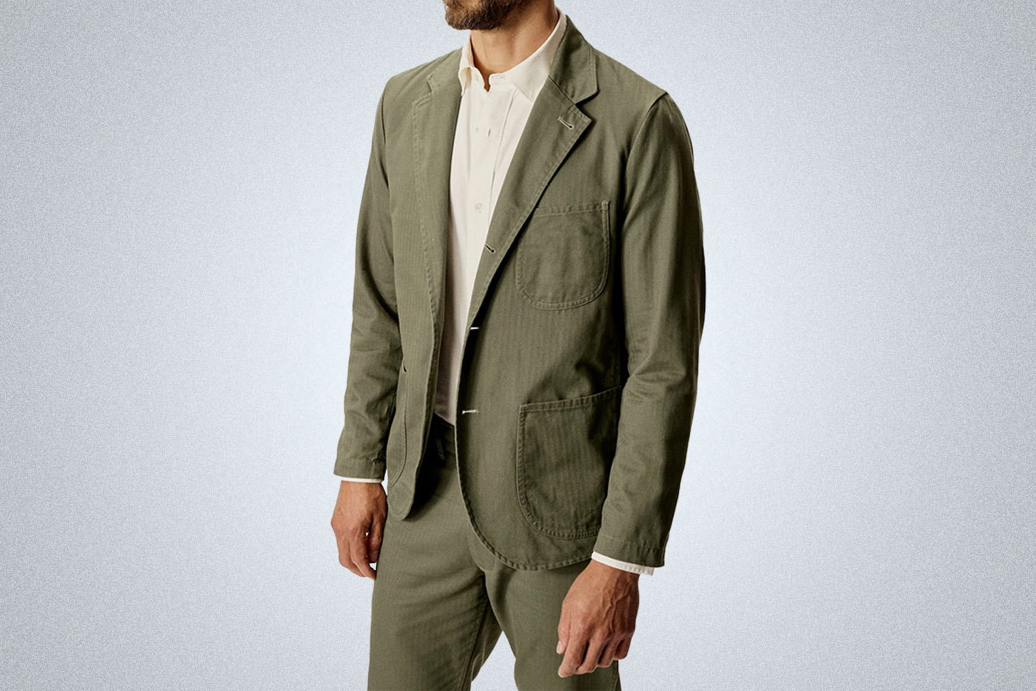 a model in a green Buck Mason travel blazer on a grey background