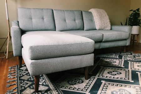 A close-up photo of a Burrow Nomad Sofa Sectional Couch in an apartment on top of a rug with a blanket draped over the back