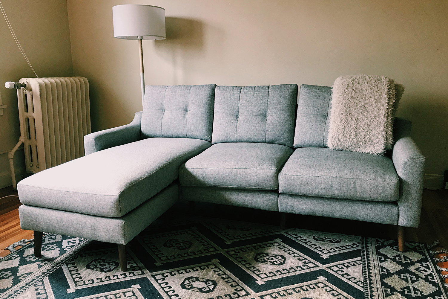 A Burrow Nomad Sofa Sectional in grey sitting on a rug with a blanket draped over the back