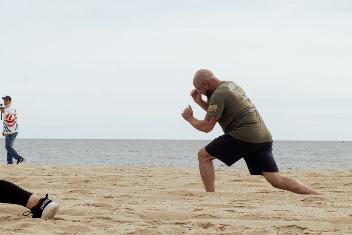 A man doing lunges in the sand while shadow-boxing.