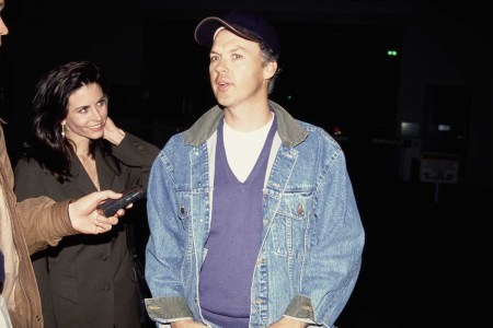 American actress Courteney Cox, wearing a black outfit, and American actor Michael Keaton, who wears a denim jacket over a blue v-neck sweater and a white t-shirt, beside a man holding a dictaphone, attend the Culver City premiere of 'Basic Instinct' at Sony Pictures Studios in Culver City, California, 18th March 1992.