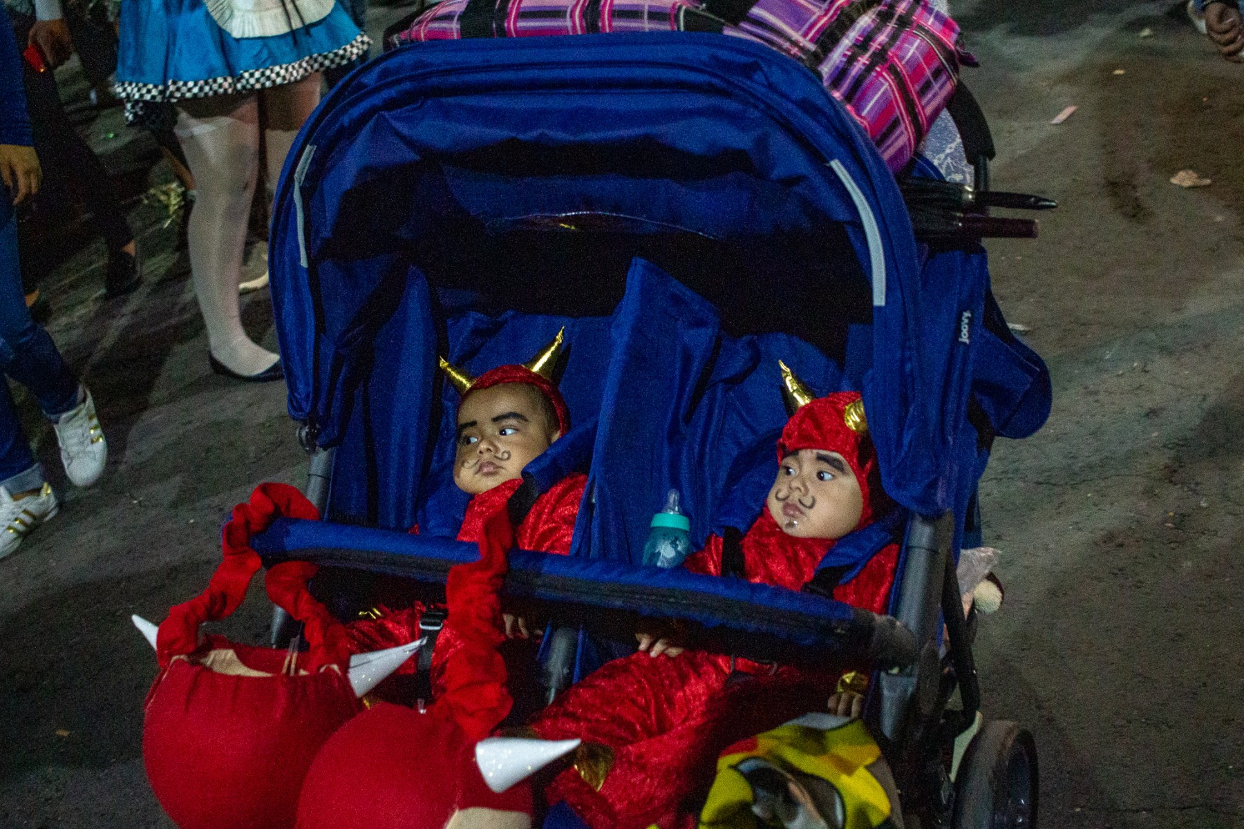 A pair of babies dressed in their finest satanic attire are wheeled along outside of the cemetery.