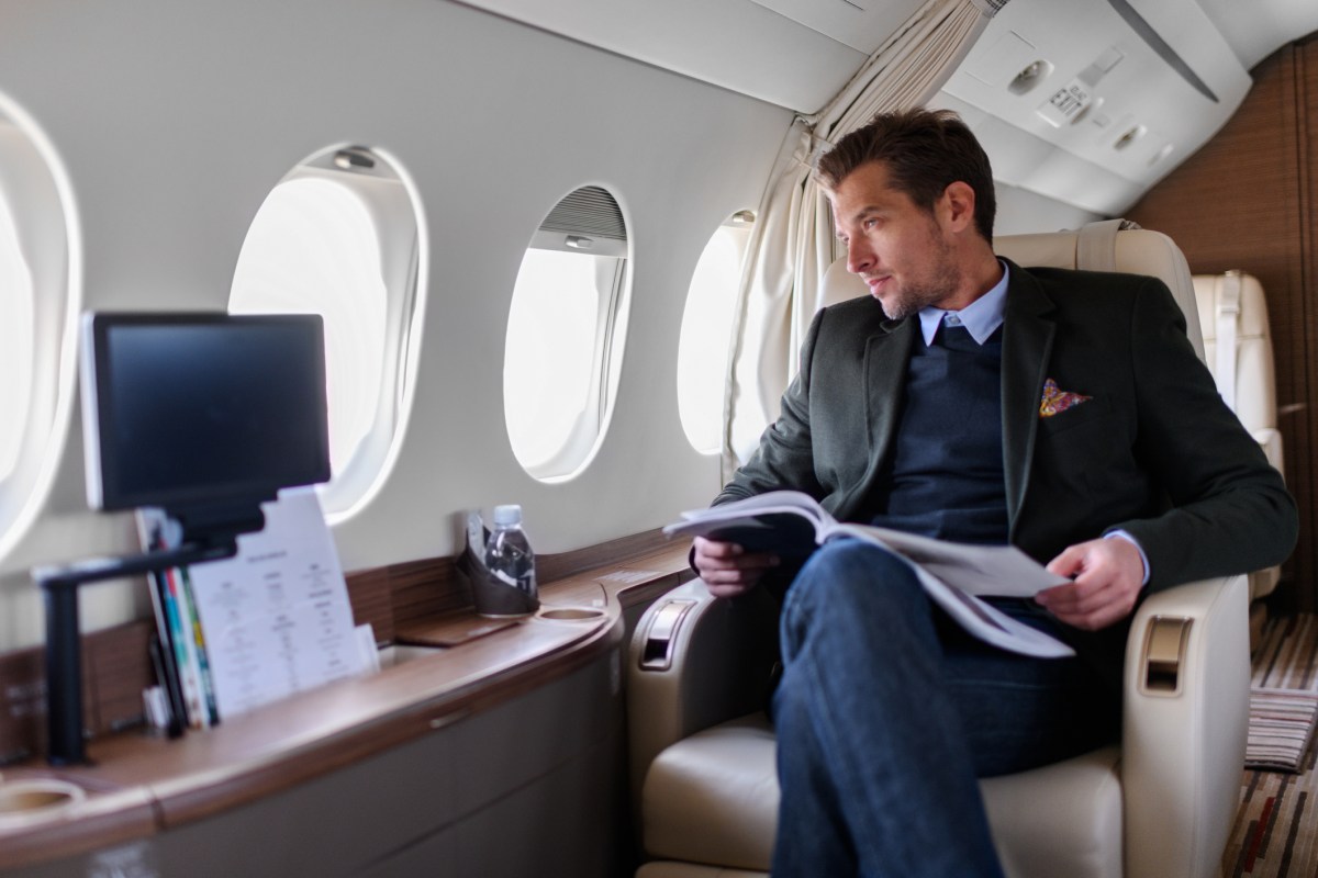 Man sitting inside private jet airplane and looking outside the window while reading a magazine.