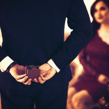 A man holds an engagement ring box behind his back