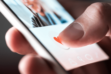 Close up photo shows someone holding a smart phone with a dating app displayed on the screen