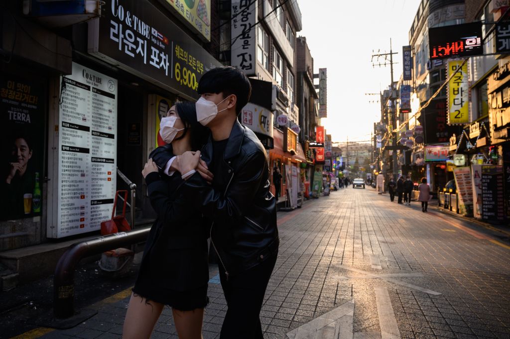 People wearing face masks amid concerns over the COVID-19 novel coronavirus, walk through an alleyway in Seoul on Marh 24, 2020. (Photo by ED JONES/AFP via Getty Images)