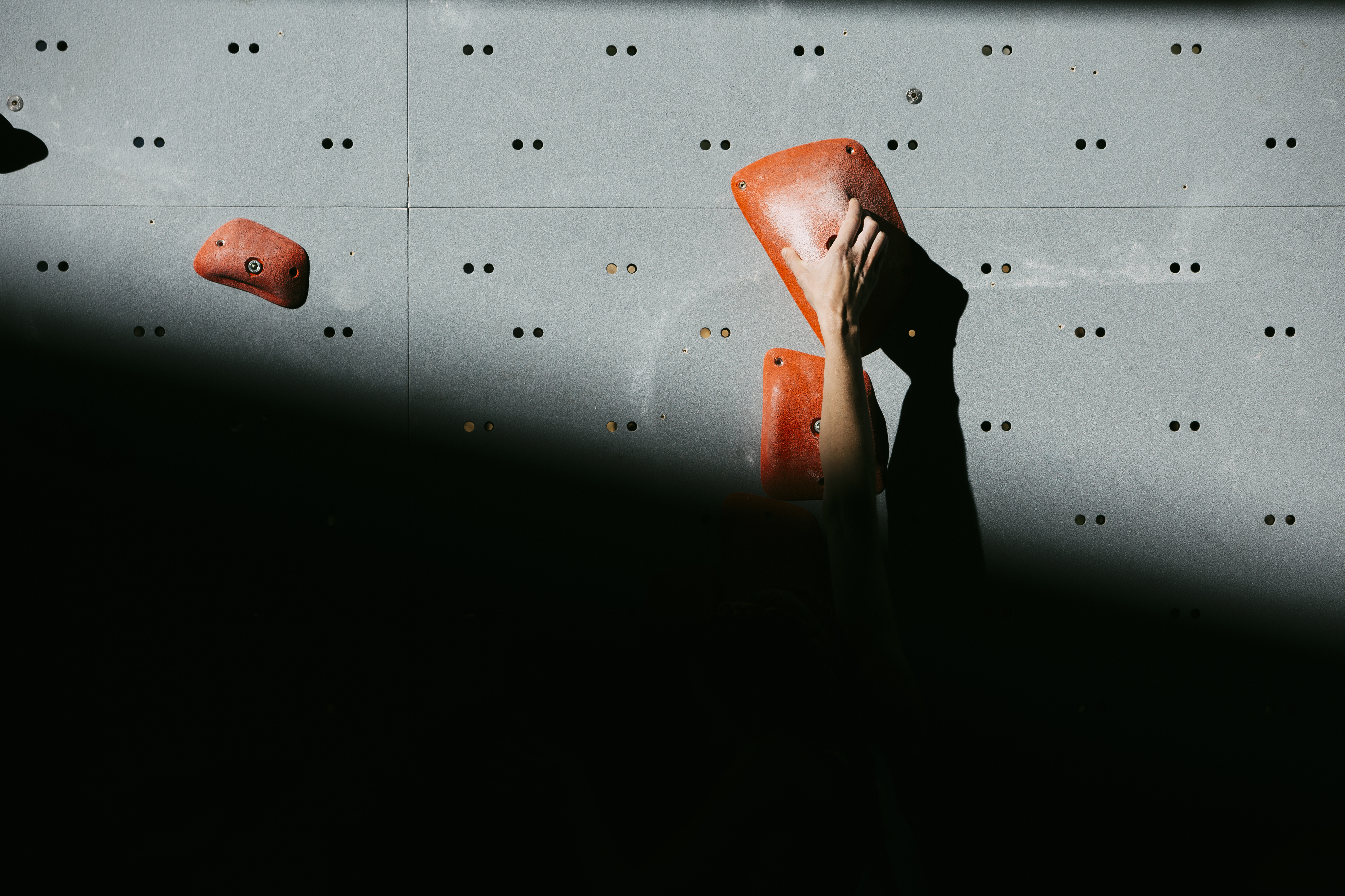 A hand reaching for a climbing hold on a rock wall.