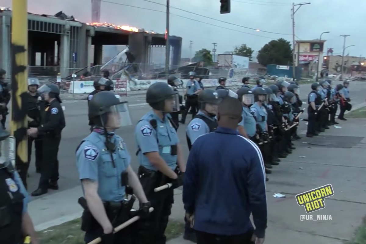 A black man walks in front of Minneapolis police officers during protests