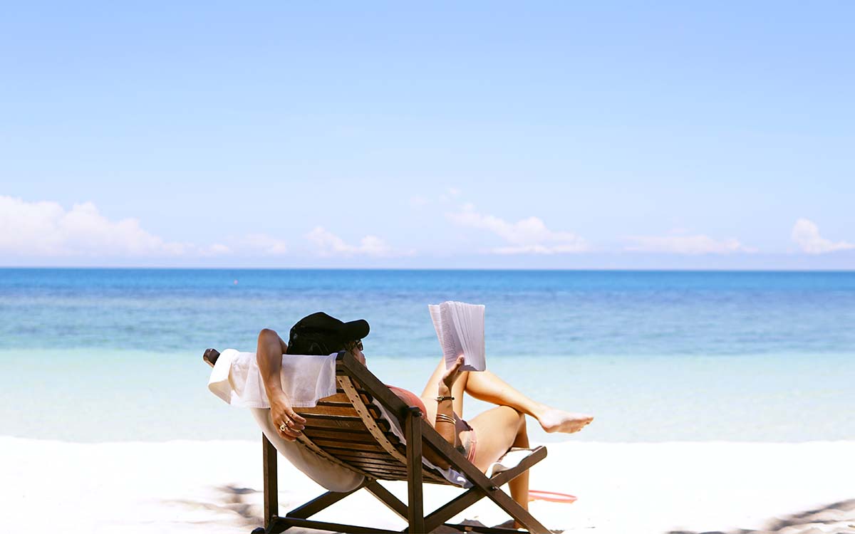 Woman laying on a sunny beach reading a book