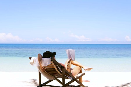 Woman laying on a sunny beach reading a book