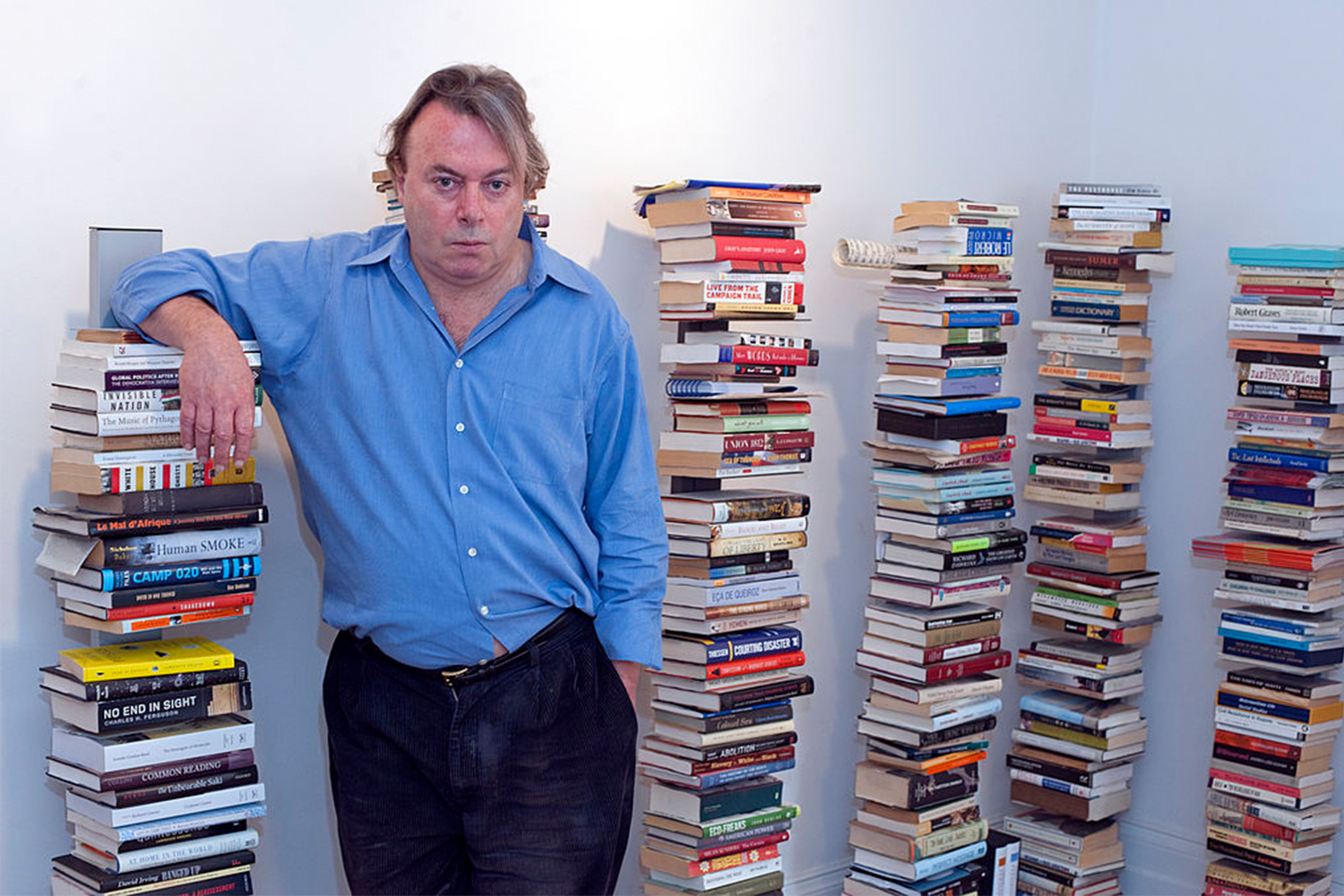 Christopher Hitchens standing next to piles of books